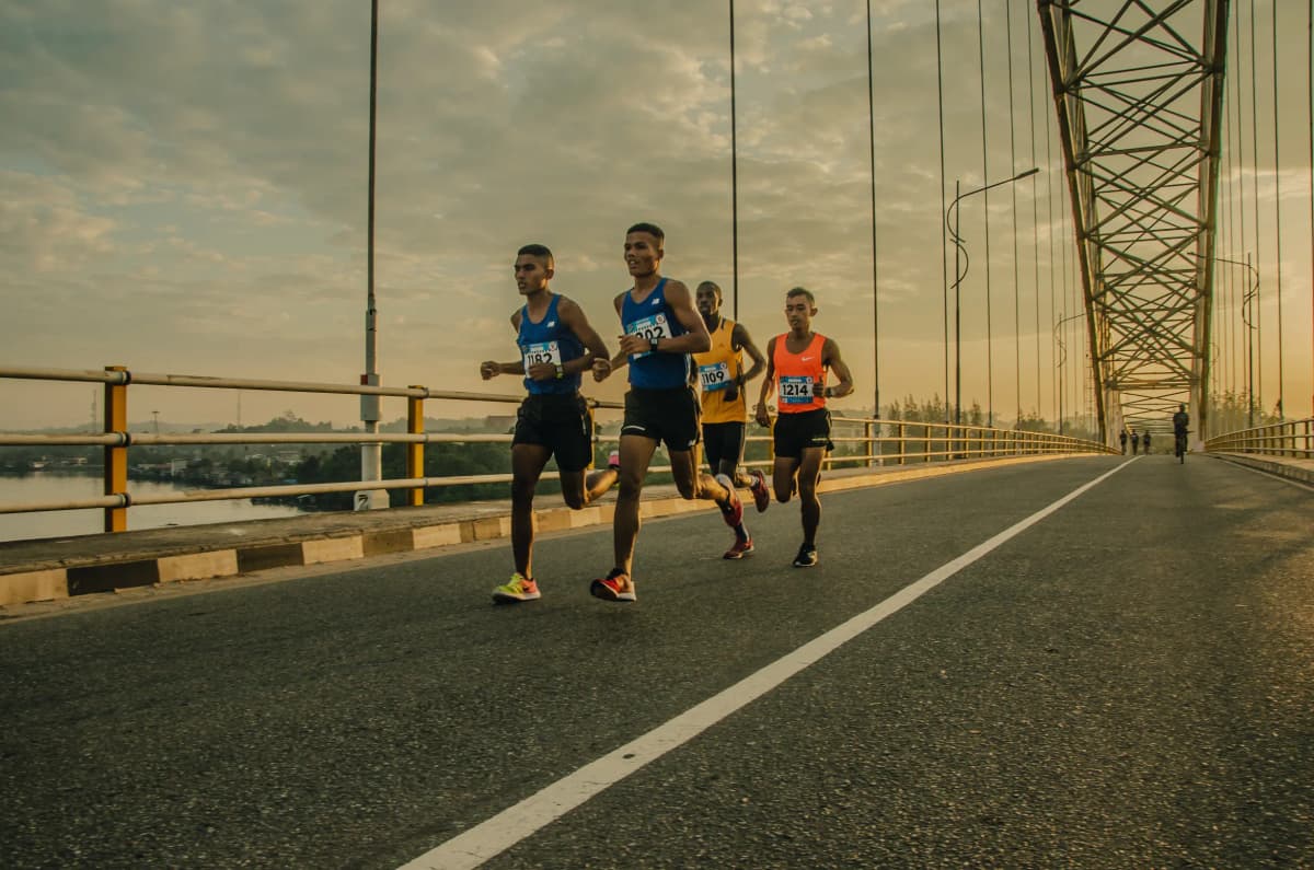 four athlete runners road running over a bridge together