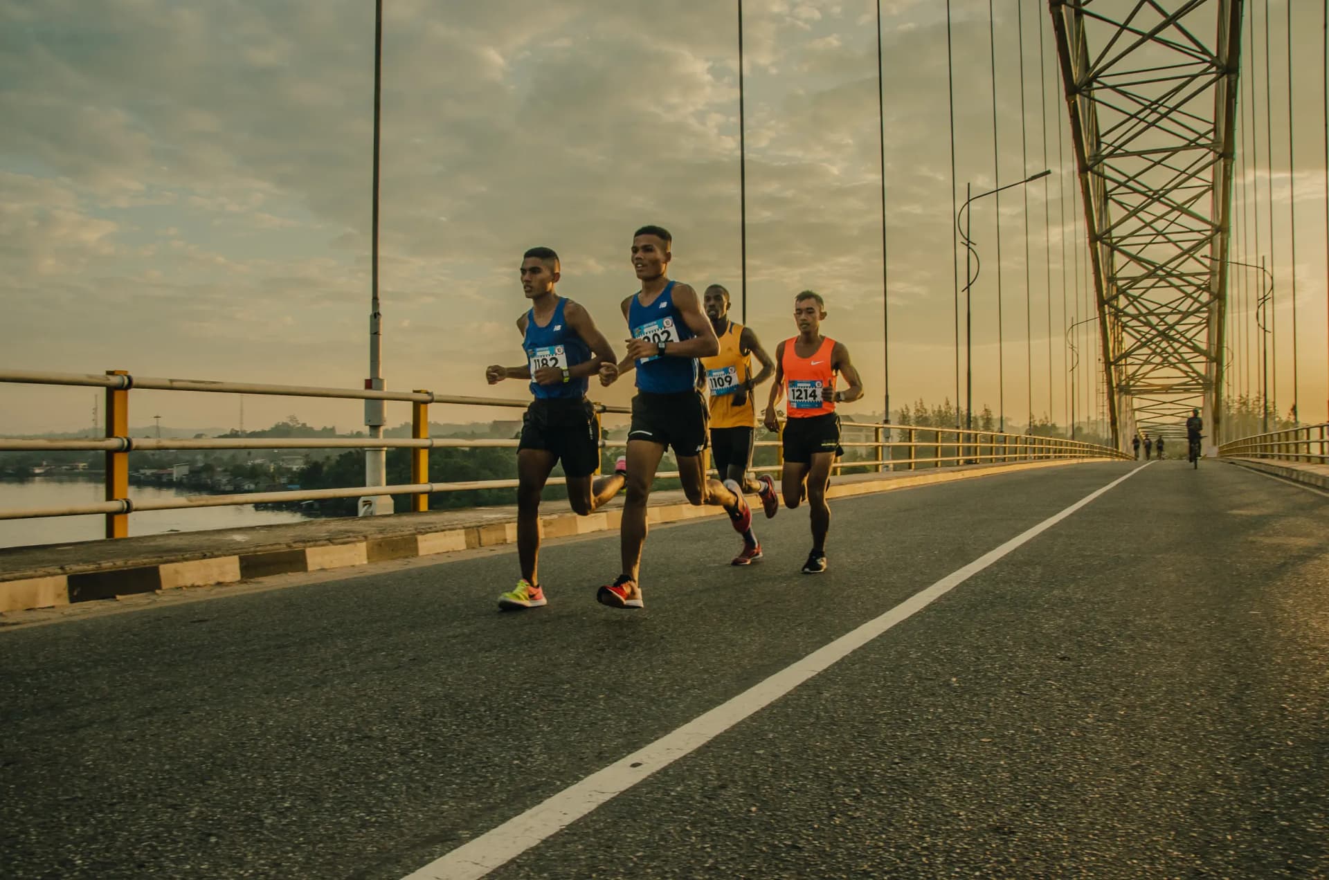 four athlete runners road running over a bridge together